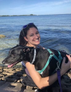 Briana Golob holding her black lab mix dog Pumba in front of a bay.