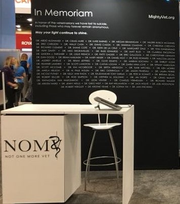 The NOMV Booth at a conference with a black wall titled "in memorium" and a list of veterinary professionals that died