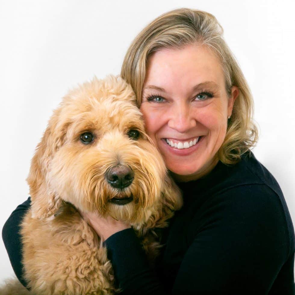 A woman smiling and holding a fluffy golden dog.