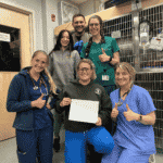 Six veterinary professionals are wearing scrubs and smiling towards the camera. Three of the people in the image are giving a "thumbs up" and the person in the front of the group holds a piece of paper that shows a "Thank You" message.